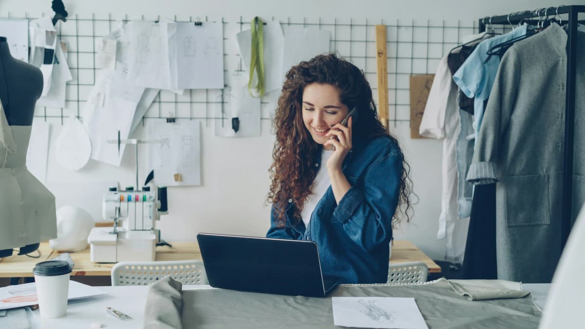Small business owner on the phone while working on a laptop in her shop